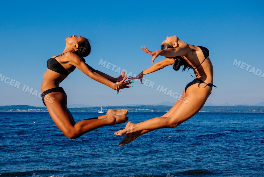 Two women performing acrobatic partner yoga jumping above water