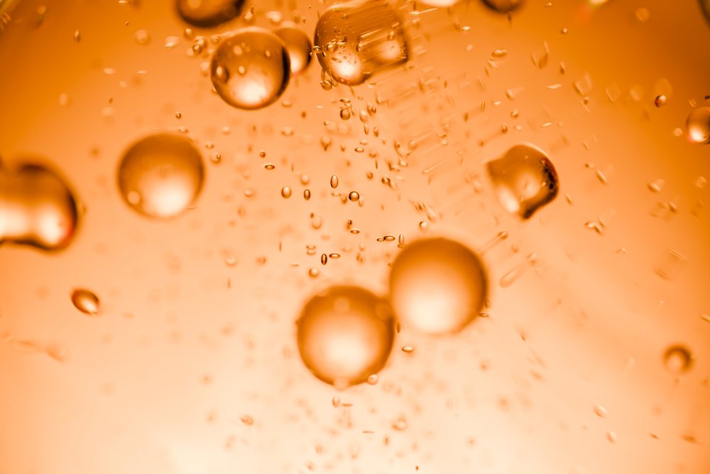 Orange liquid bubbles suspended and floating in a bright, abstract macro background.