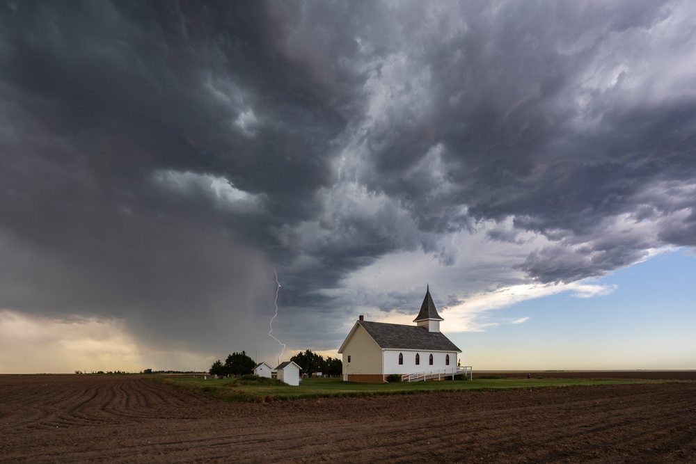 Lightning bolt strikes near a rural Church under dark storm clouds with a plowed farm field, Oshkosh, Nebraska, USA.