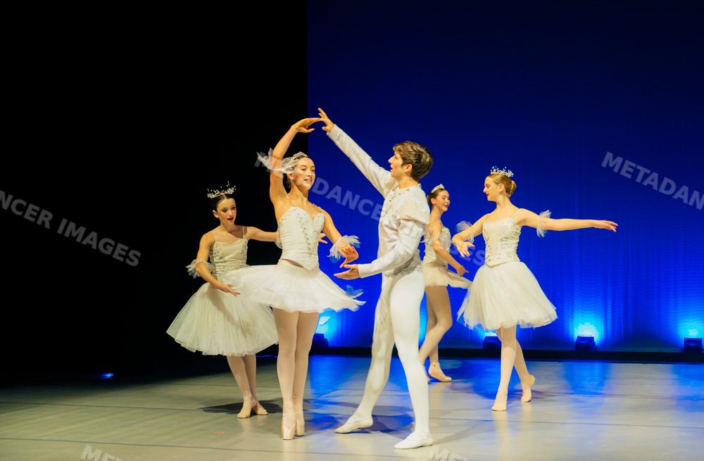Ballet dancers perform a classical routine on stage with blue lighting