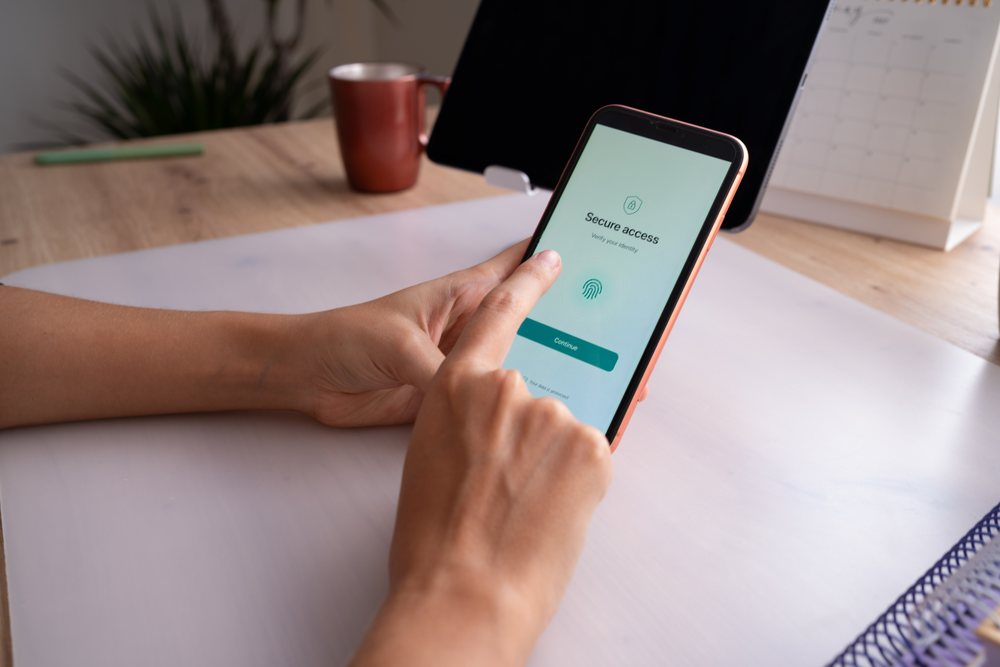 Person verifying identity using fingerprint on smartphone desk setup, home, girl, Spain.