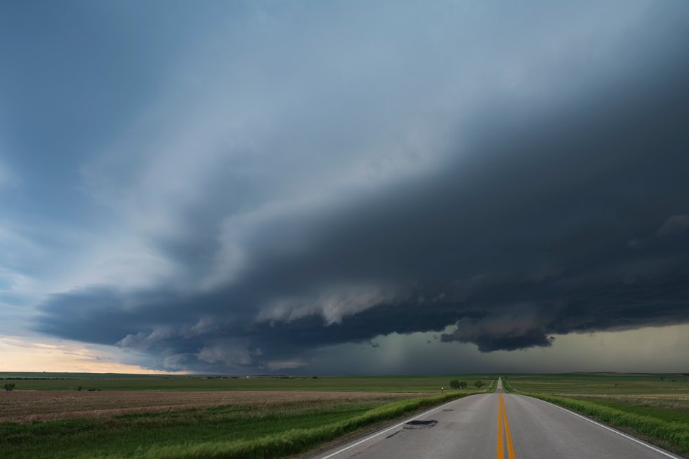 High Base Storm with dark clouds approaches across open grassland fields along a rural asphalt road, Storm Chasing, Weather, Environmental, Wood, South Dakota, USA.