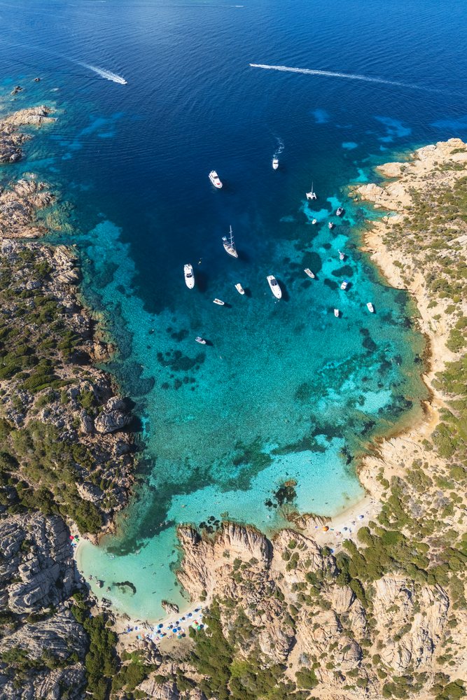 Boats anchored in clear blue waters of Cala Napolatana cove at a rocky coast with small sandy beaches, Travel Images, La Maddalena, Sardinia, Italy.
