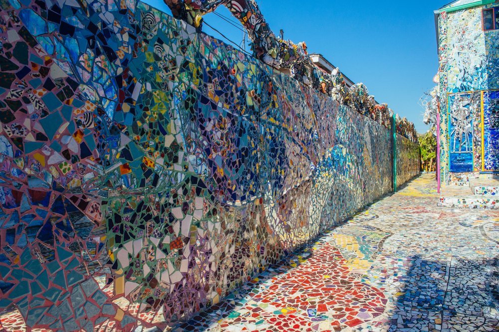 Colorful mosaic tile artwork decorates walls and pathway under blue sky in an outdoor art installation, CA, USA.