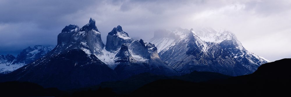 Los Cuernos mountains with snow caps rise above Lake Pehoe under a cloudy sky, Chile.