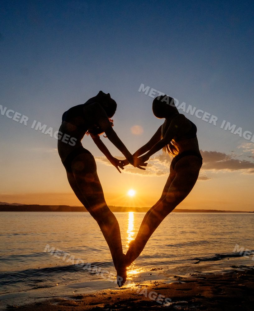Two white women doing partner acrobatics yoga at sunset on a beach