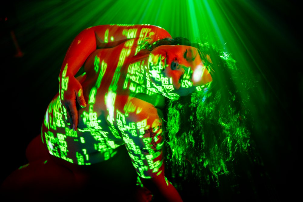 Pregnant woman with curly hair posed in side view under artistic green numeric projections and red lighting on a dark background, pregnancy.