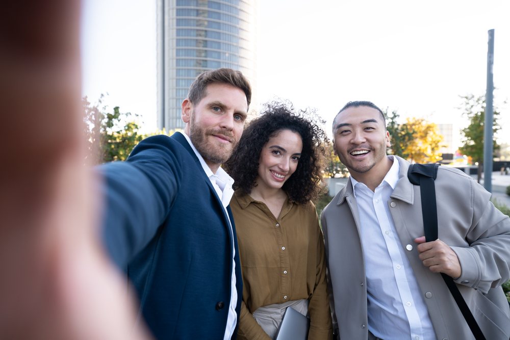 Three people smiling and taking a selfie outdoors near an office building, Madrid, Spain.
