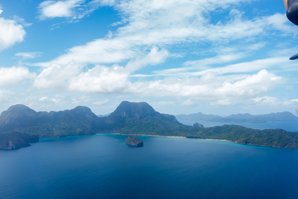 Island coastline with blue ocean waters and partly cloudy sky, Philippines.