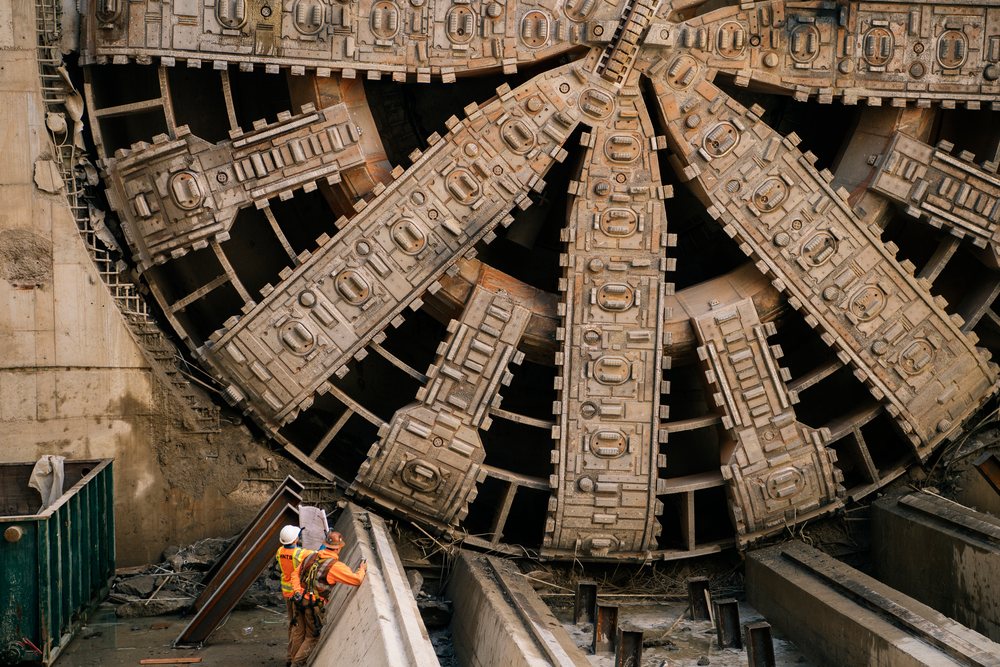 Two construction workers examine plans beside a large tunnel boring machine at a construction site, large tunnel boring machine, drilling, USA.