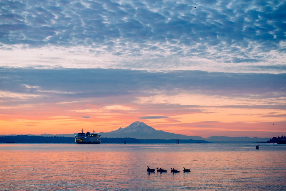 Ferry crosses calm water at sunset with Mount Rainier visible in the background, Bainbridge Island, WA, USA.