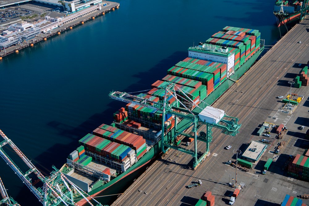 Container ship loaded with colorful containers docked with cranes unloading cargo, Port of Long Beach, CA, USA.