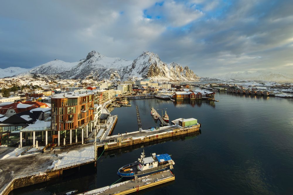 Sunrise over the port, showing snow-covered mountains including Goat Mountain and calm water reflecting the sky, Landscape, Svolvaer, Norway.