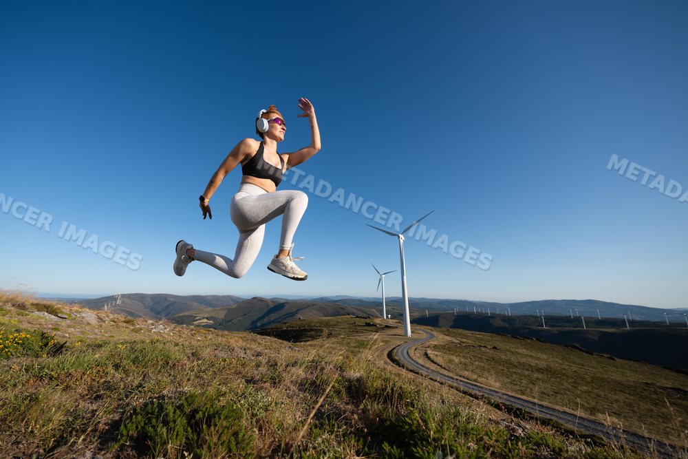 A young white woman jumps energetically on a mountain trail with wind