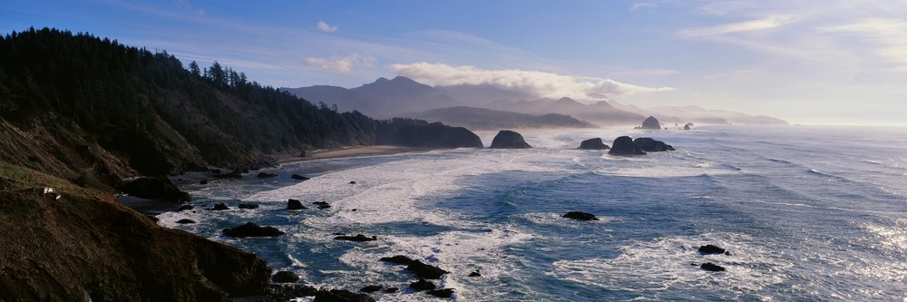 Waves crash along Cannon Beach's rocky shoreline with forested hillsides and rock formations at Ecola State Park, Oregon, Ecola State Park Oregon, USA.