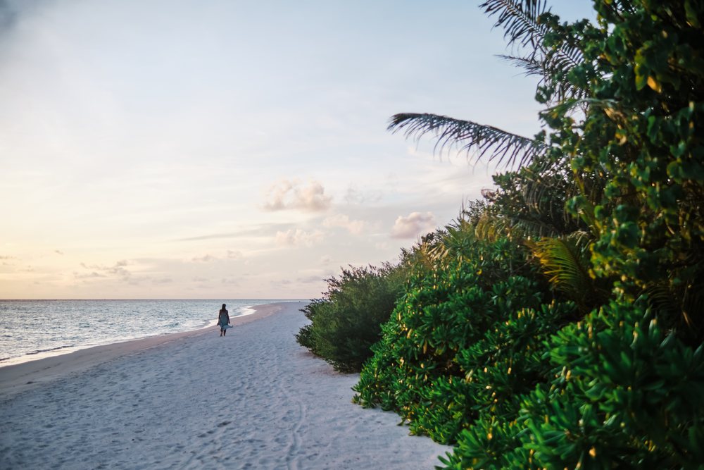 A woman walking along a tropical beach at sunset in the Maldives