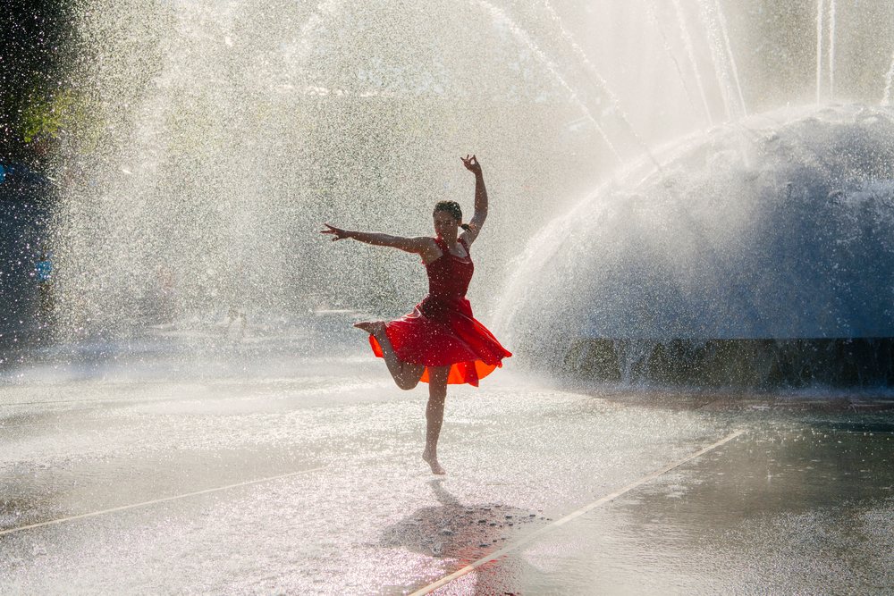 Woman dancing barefoot in water spray from fountain outdoors on a sunny summer day, USA.