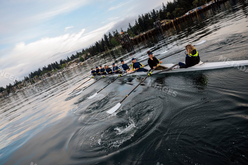 A white women's rowing team practicing rowing on calm coastal waters