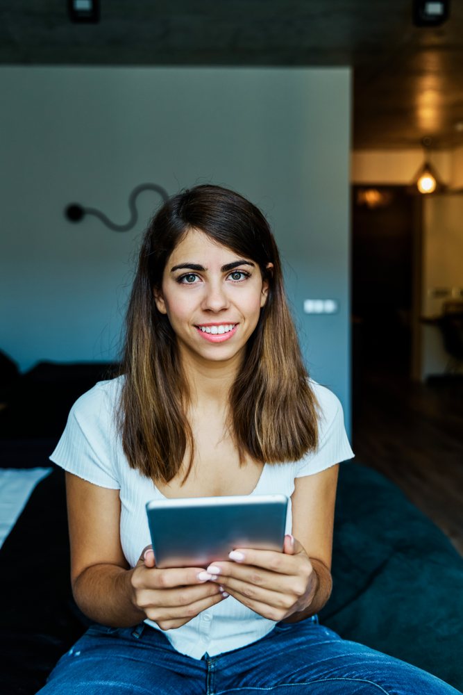 A young woman holding a tablet and smiling indoors in a hotel