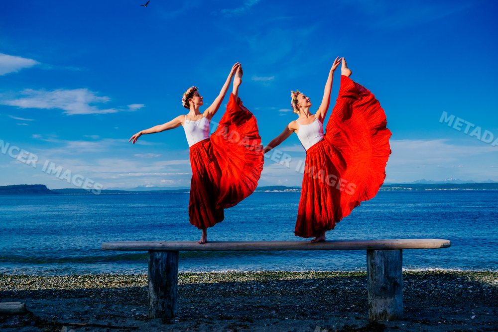 Two white women performing partner acrobatics yoga poses by the water