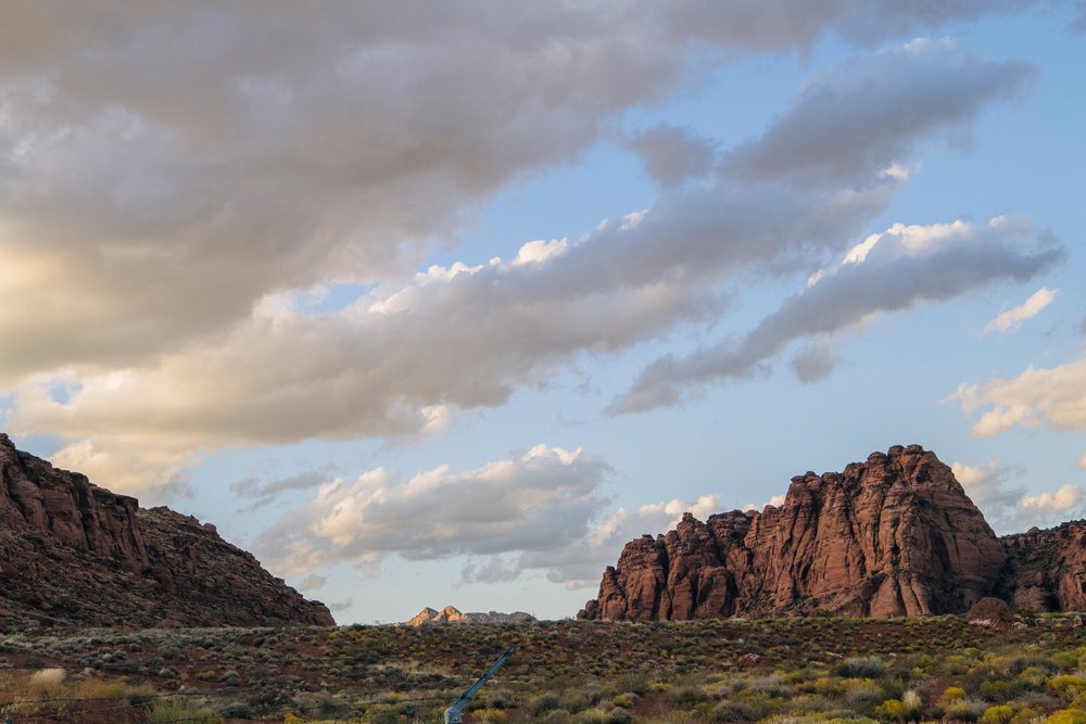 Rock formations of red Cliffs Desert rise over scrub vegetation under a cloudy sky, Snow Canyon, Utah, USA.