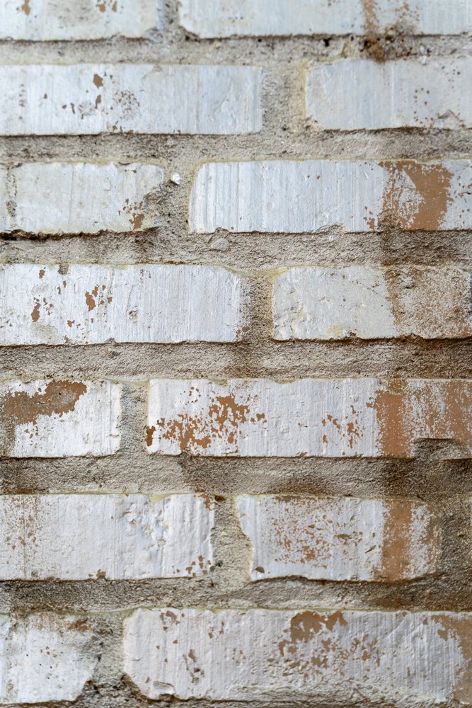 White painted brick wall with weathered cement mortar and brown paint spots on its rough exterior surface, texture, abstract texture, background, wallpaper, Spain.