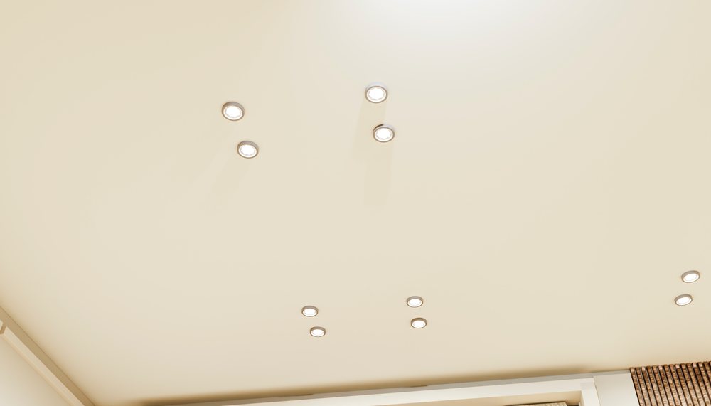 White ceiling with multiple recessed downlights illuminating a minimalist interior space.