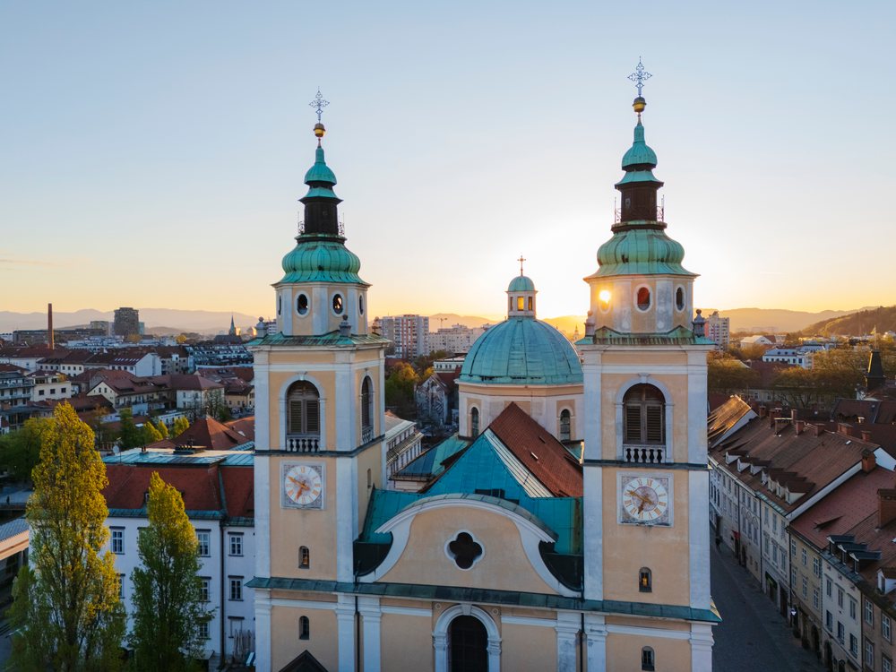 St Nicholas' Cathedral, is prominent at sunset with twin clock towers, central dome, and crosses over the city skyline, landscape, cityscape, Ljubljana, Slovenia.