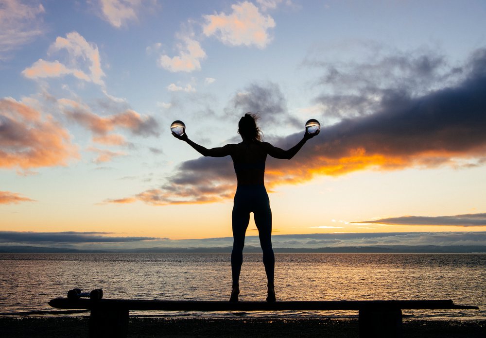 Silhouette of a woman balancing glass balls at sunset by a peaceful lake in Washington state, USA.