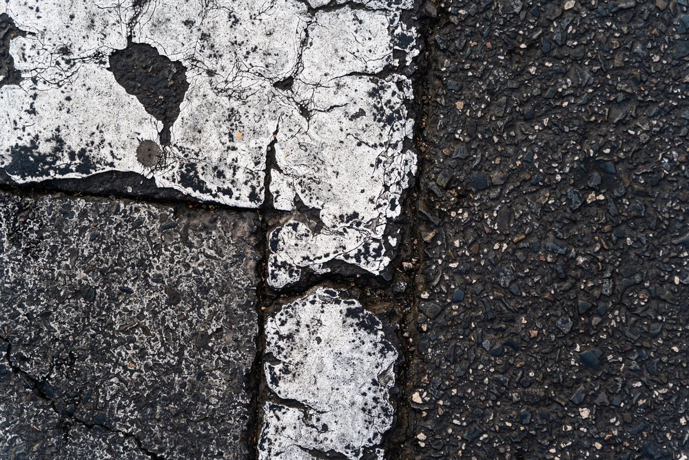 Close-up view of worn, cracked white road markings on textured asphalt pavement in an urban environment, texture, abstract texture, background, wallpaper, Spain.