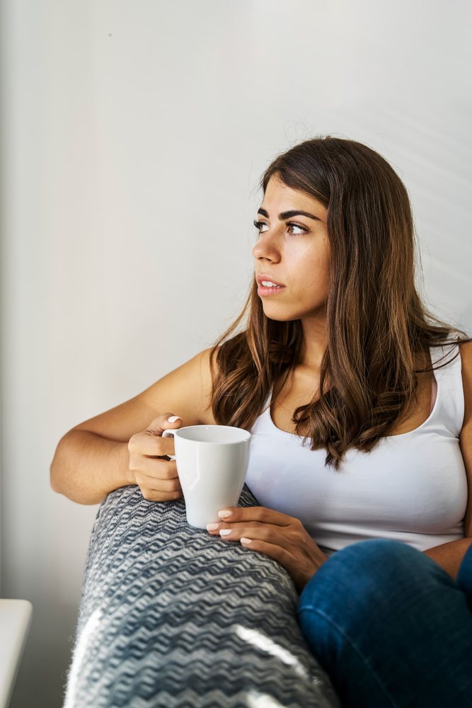 Young white woman holding a cup and looking pensively indoors