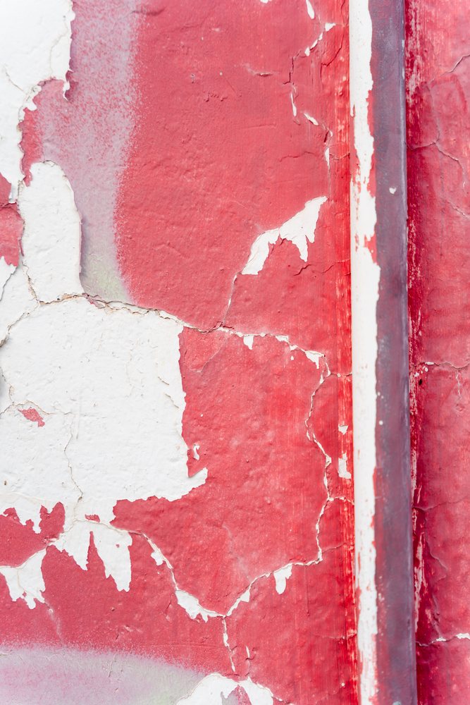 Close-up of peeling red and white paint with cracks and flakes on a weathered outdoor wall, texture, abstract texture, background, wallpaper, Spain.