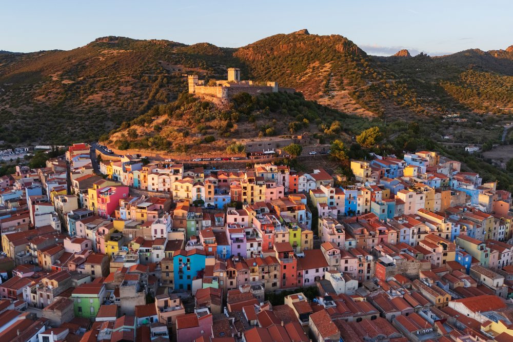 Aerial Sunset view shows colorful houses clustered in Bosa village below a hilltop castle, Travel Images, Sardinia, Italy.