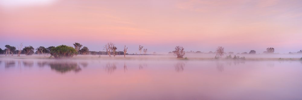 Mist rises over a calm lake with trees reflected in the water at sunrise, Kakadu National Park Northern Territory, Australia.