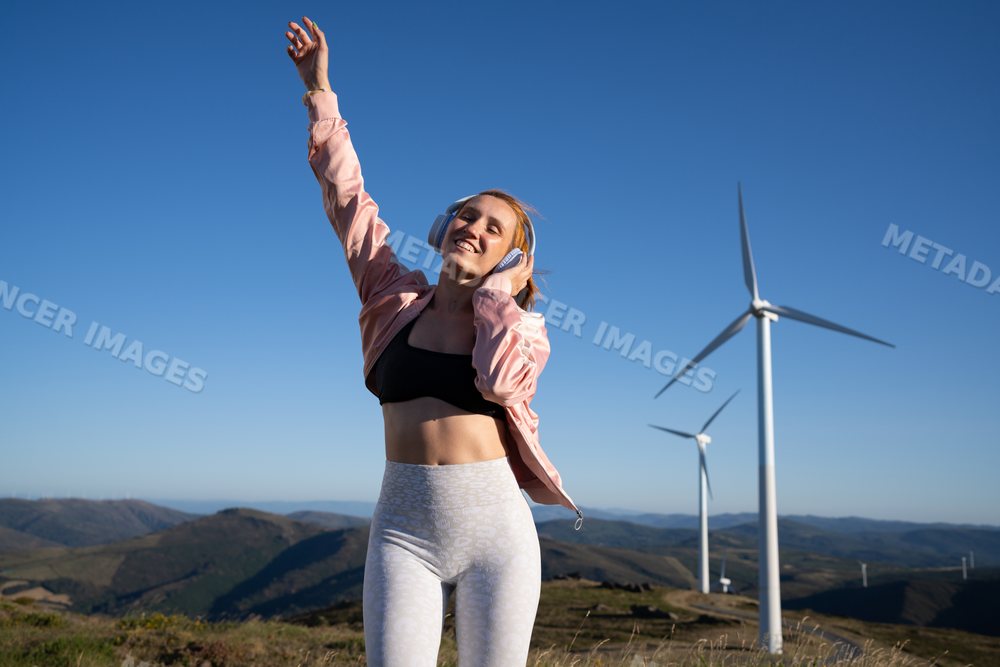 White woman enjoying music outdoors near wind turbines in Galicia