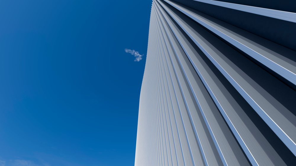 Modern steel and glass skyscraper rises against a clear blue sky with a small cloud nearby.