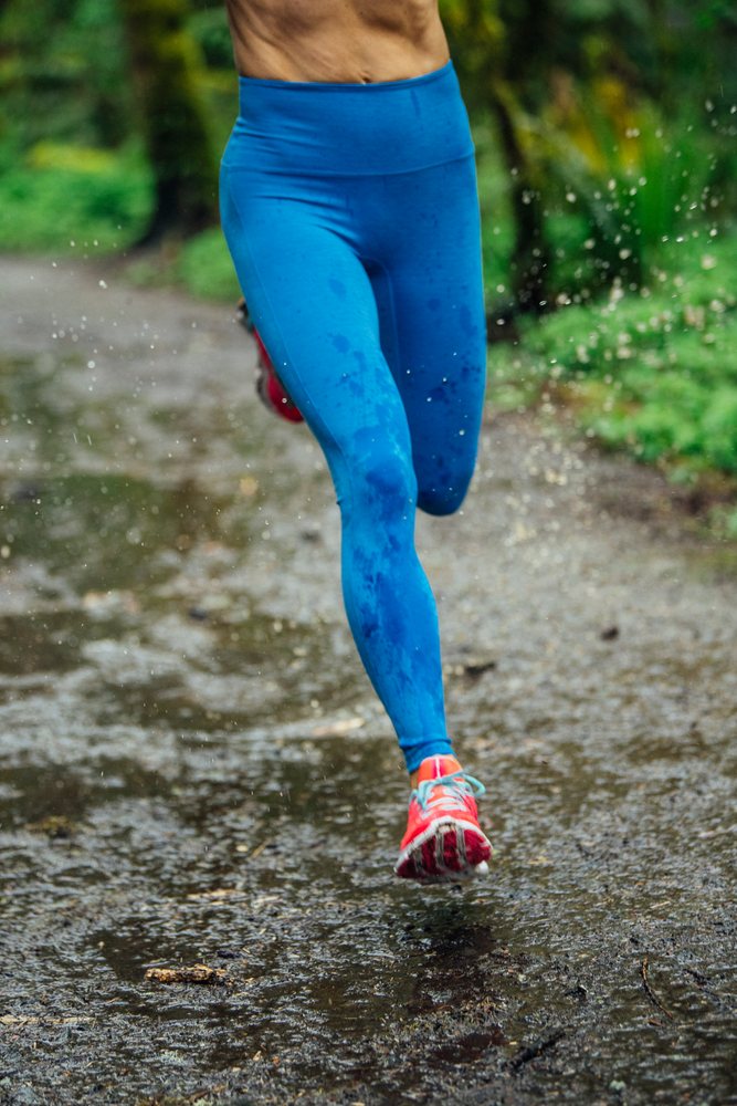 Runner in blue leggings and orange shoes splashes water while running on a wet trail, Calisthenics, USA.