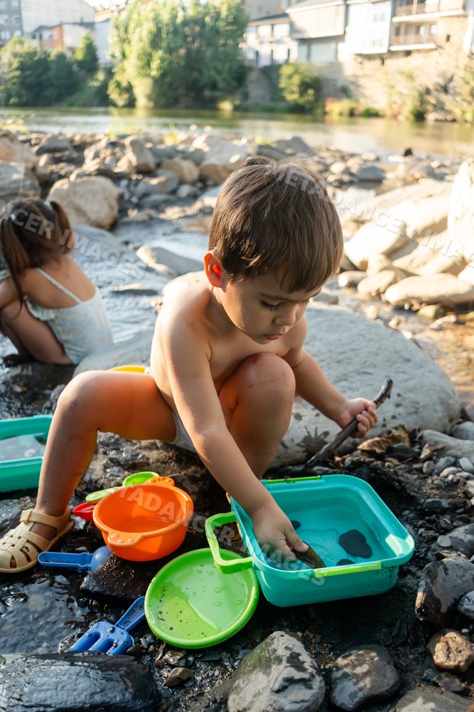 A young white boy playing with colorful toys by a rocky riverbank