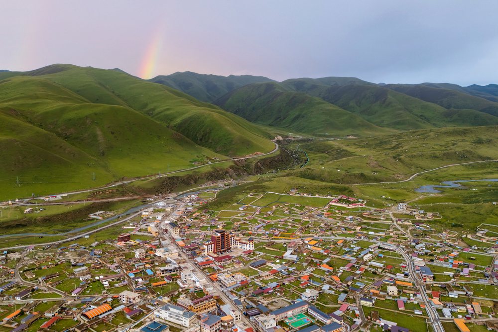 Zhuqing village nestled in green mountains near a river under a Sunset sky with a rainbow, Sechuan Province, People's Republic of China.