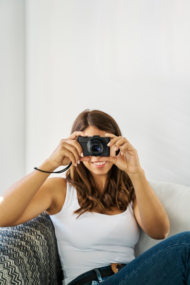 A young white woman takes a photo with a digital camera indoors