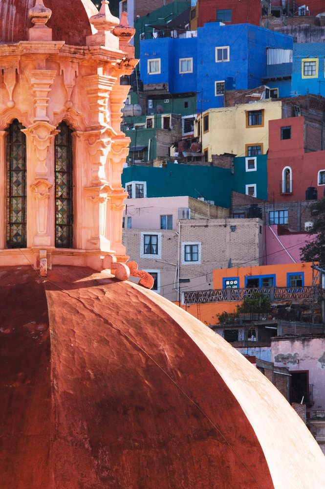 Orange church dome with stained glass windows stands before multi-colored houses on a hillside, Guanajuato, Mexico.