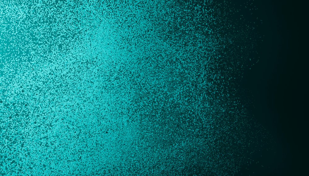Close-up view of dense small aqua-colored bubbles and foam on a liquid surface showing textured water pattern.