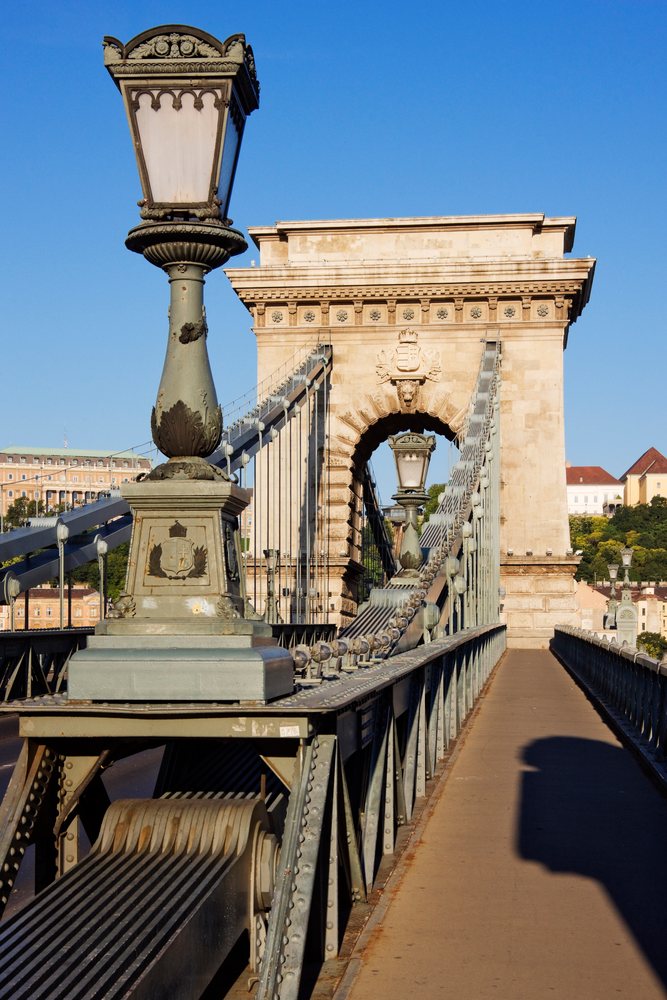 Historic Chain Bridge with metal structure and lanterns spans the Danube River, Hungary under a clear sky, Budapest.