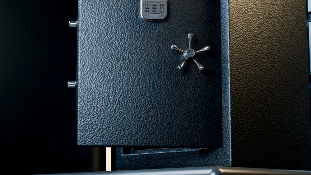 Metal safe with slightly open door showing combination keypad and six-spoke metal handle in dark setting.
