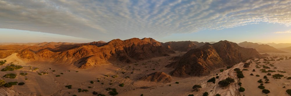 Sunrise over Hoanib River Valley in Namibia's Kunene Region reveals rugged desert mountains, rocky terrain, and scattered desert vegetation in a dry riverbed valley, landscape, wildlife.