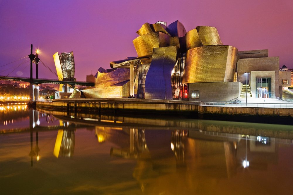 Guggenheim Museum Bilbao illuminated at night with purple sky and its reflection on the river, Spain.