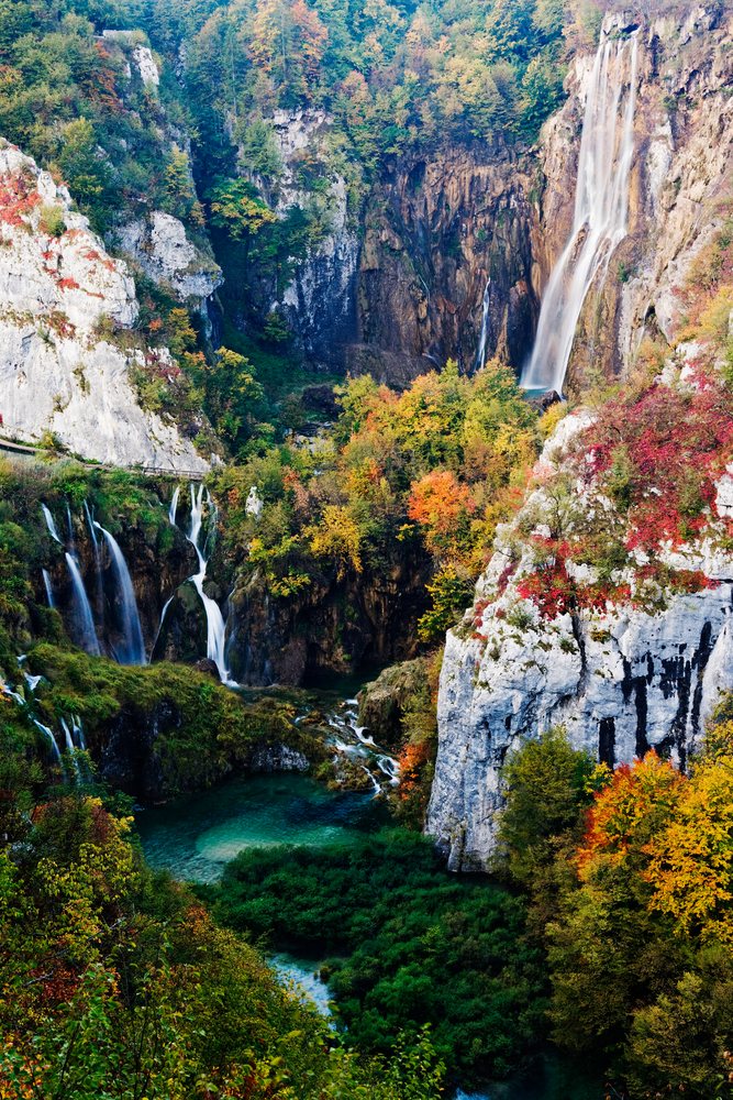 Waterfalls cascade over rock cliffs within a colorful autumn forest landscape, Plitvice Lakes National Park, Croatia.