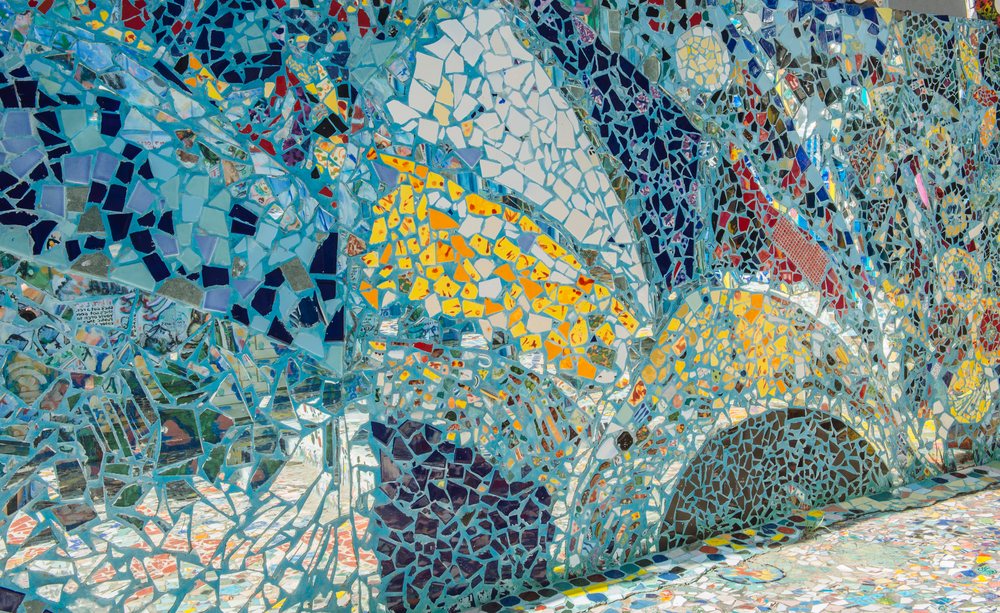 Colorful broken tile pieces form an abstract mosaic artwork covering a wall and ground surface in California, USA.