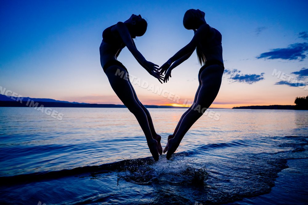 Two white women practicing partner acrobatics yoga jumping