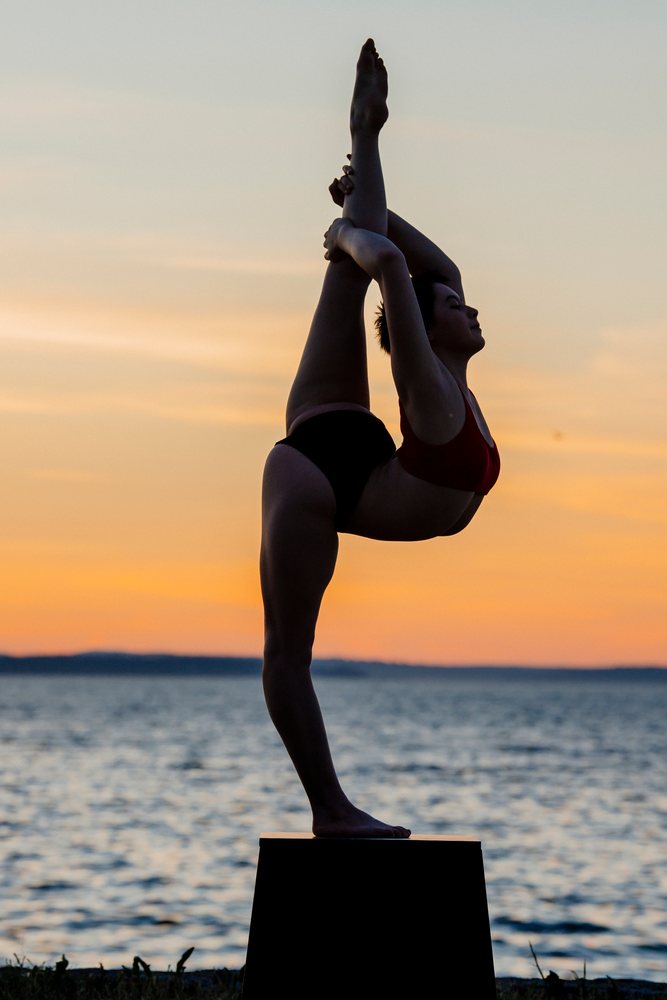 Woman practicing yoga balancing in a stretching pose outdoors at sunset by the sea, USA.